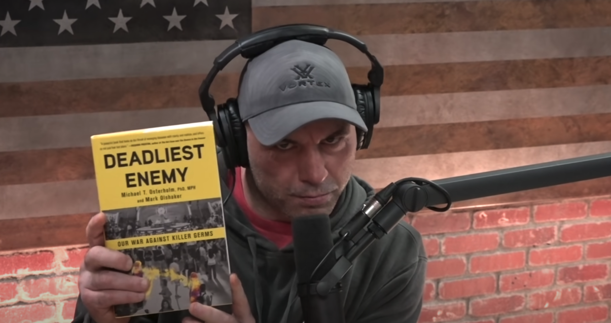 Joe Rogan holds up Michael Osterholm's book for his audience. Osterholm sits on Biden's Covid-19 advisory board. Screenshot: YouTube / PowerfulJRE