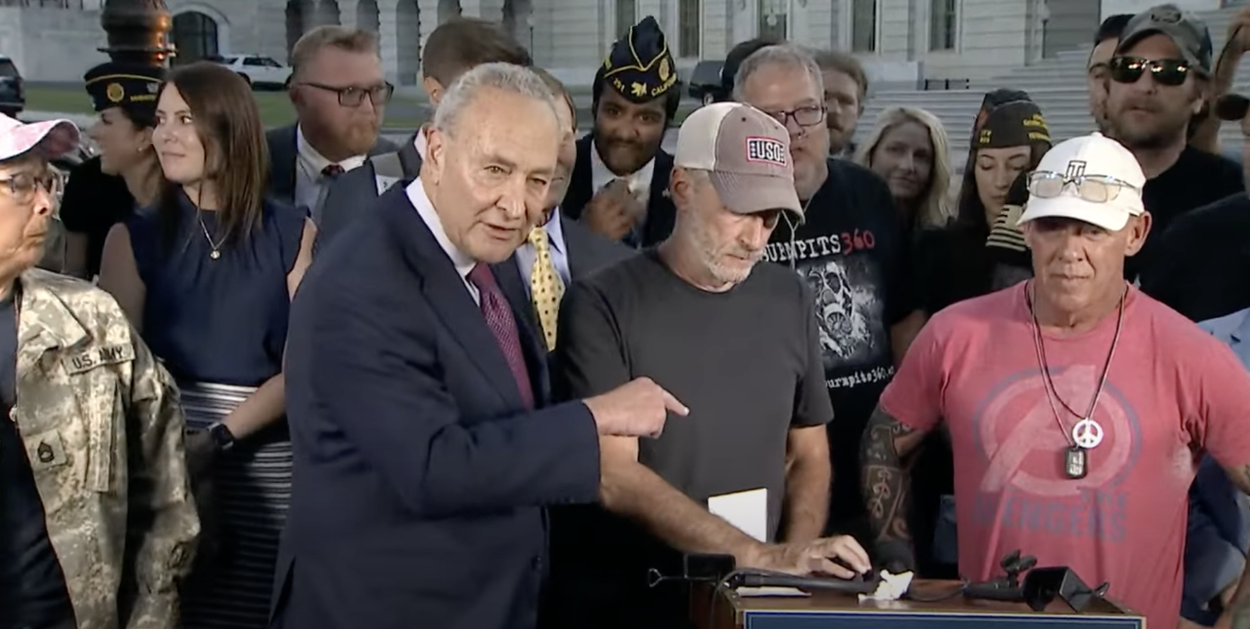 Chuck Schumer (left), Jon Stewart (center) and veterans celebrate the passage of the PACT Act. Image: PBS News screenshot