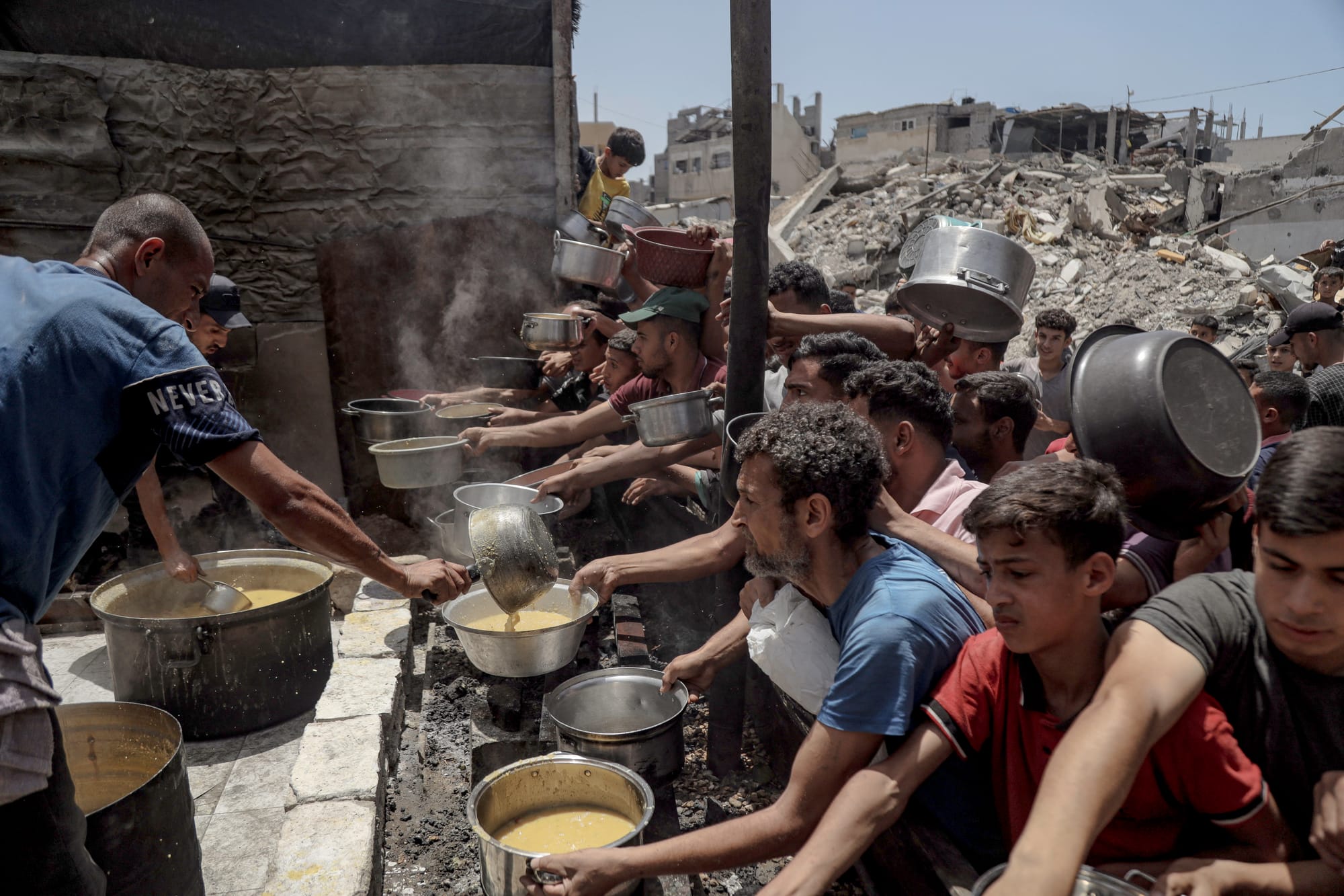 People reach out with pots during a food distribution in Jabalia Refugee Camp in Gaza City, Gaza | Photo by Abood Abusalama via Getty Images