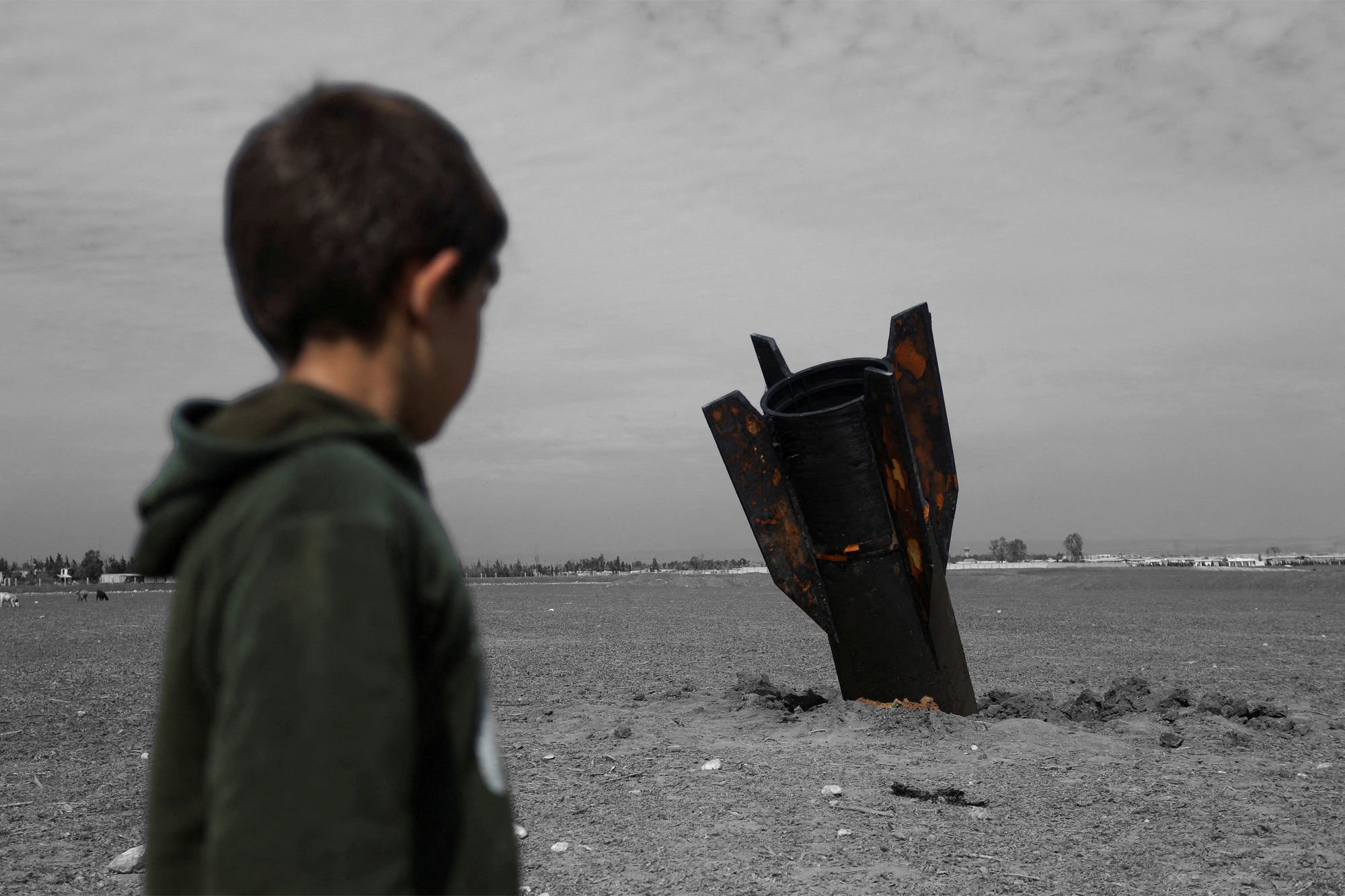 A child stands next to a missile in Qamishli, Syria — March 4, 2026 | REUTERS/Orhan Qereman, edited by Russell Nystro