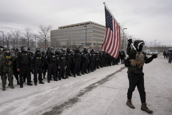 A counter-protester with a U.S. flag in front of Immigration and Customs Enforcement (ICE) agents, outside the Whipple Federal Building in Minneapolis, Minnesota | REUTERS/Tim Evans