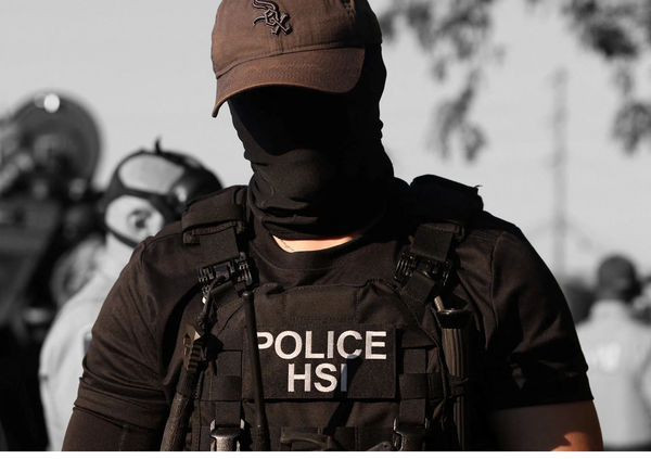 A member of Homeland Security Investigations watches as people protest outside a U.S. Immigration and Customs Enforcement facility | REUTERS/Jim Vondruska, edited by Russell Nystrom